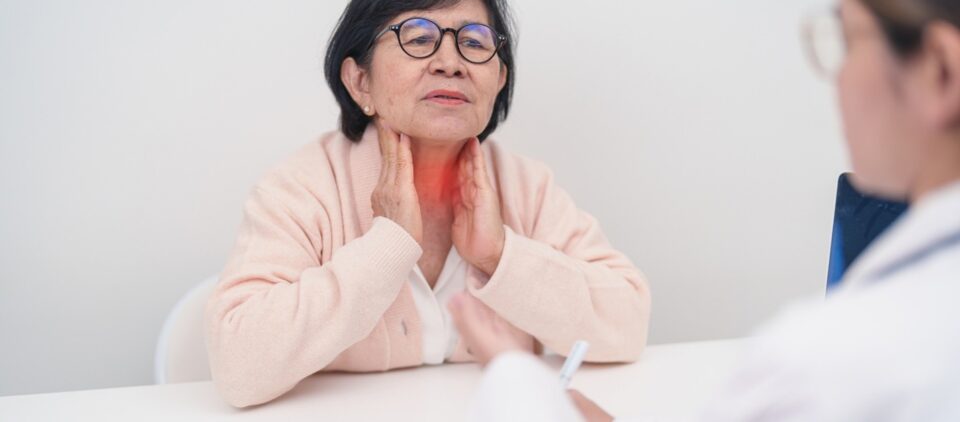Individual seated at a table holding the front of the neck while speaking with a healthcare professional in Lake Saint Louis, MO