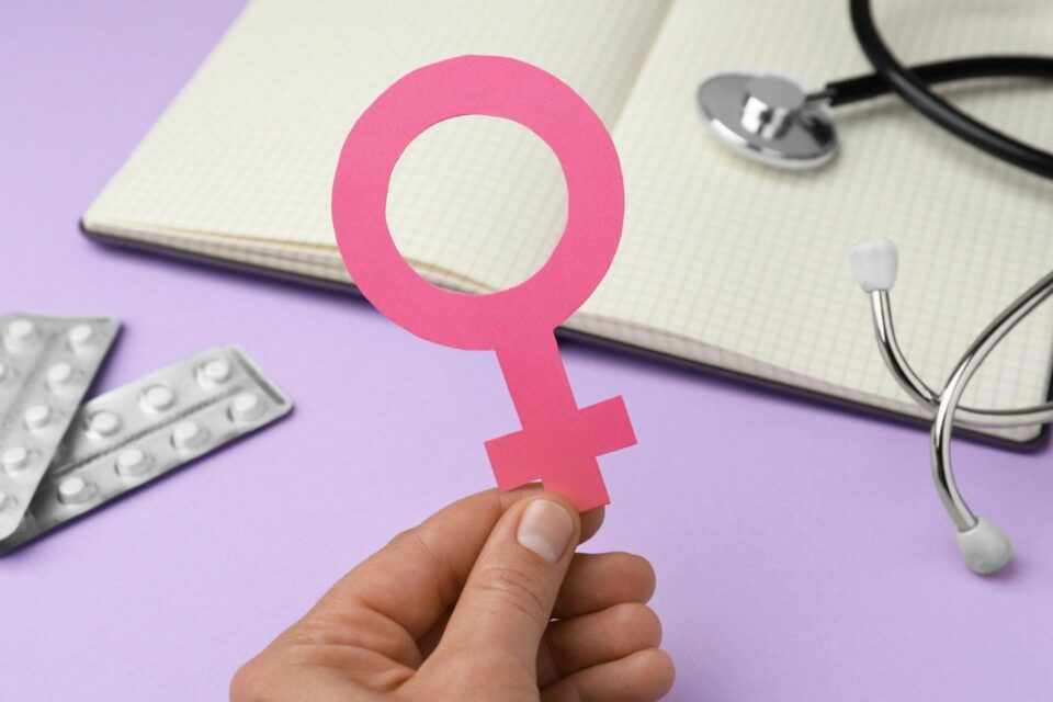 Hand holding a pink female gender symbol in front of a notebook, stethoscope in Lake Saint Louis, MO